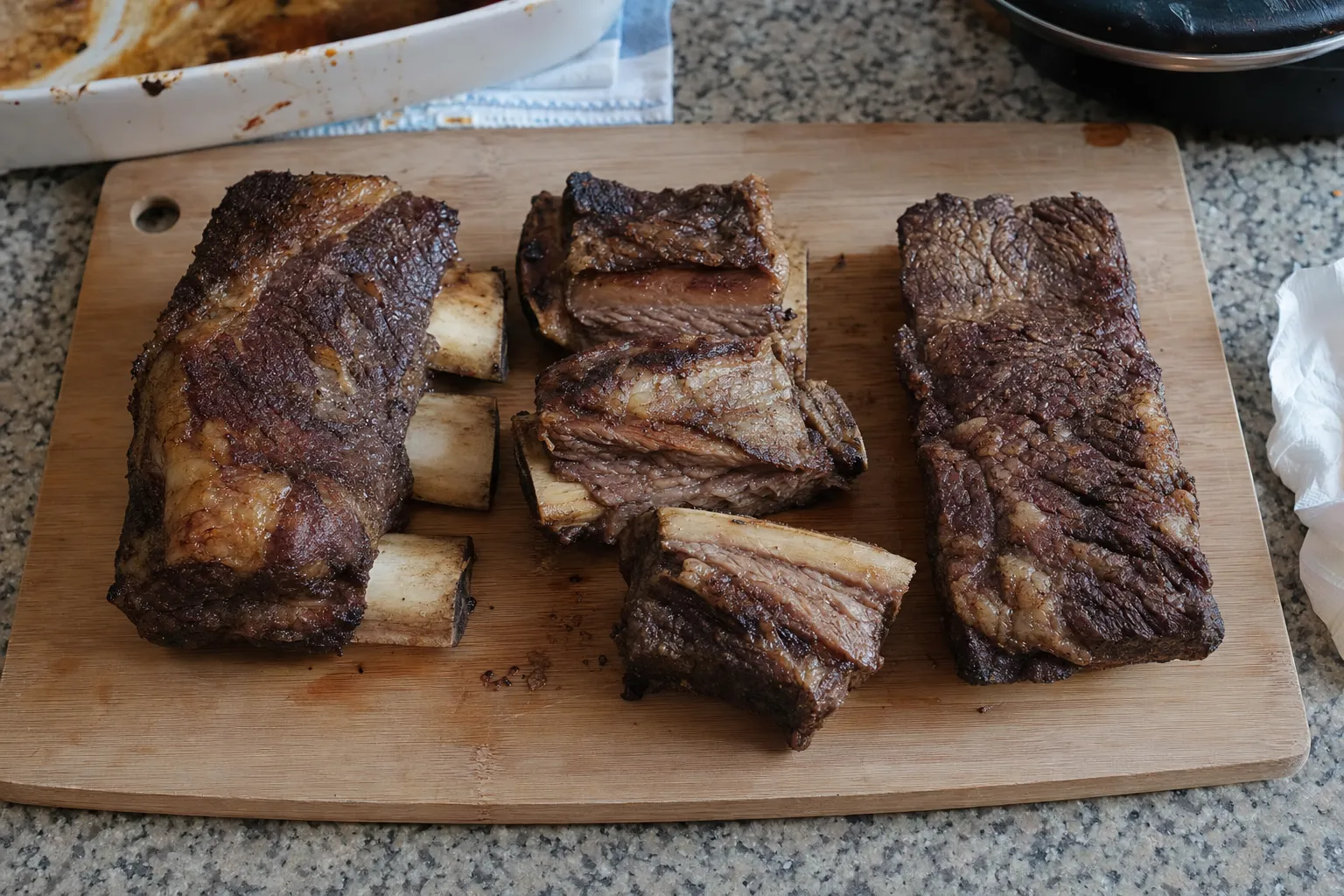 木のまな板に並べた焼いたショートリブ。左は骨3本付きのブロック、中央は骨ごと切った角切り、右は骨なしのブロック