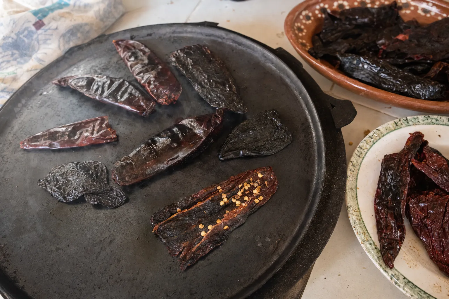 丸い鉄板で焼いている乾燥唐辛子と、横の器に盛った焼く前の乾燥唐辛子